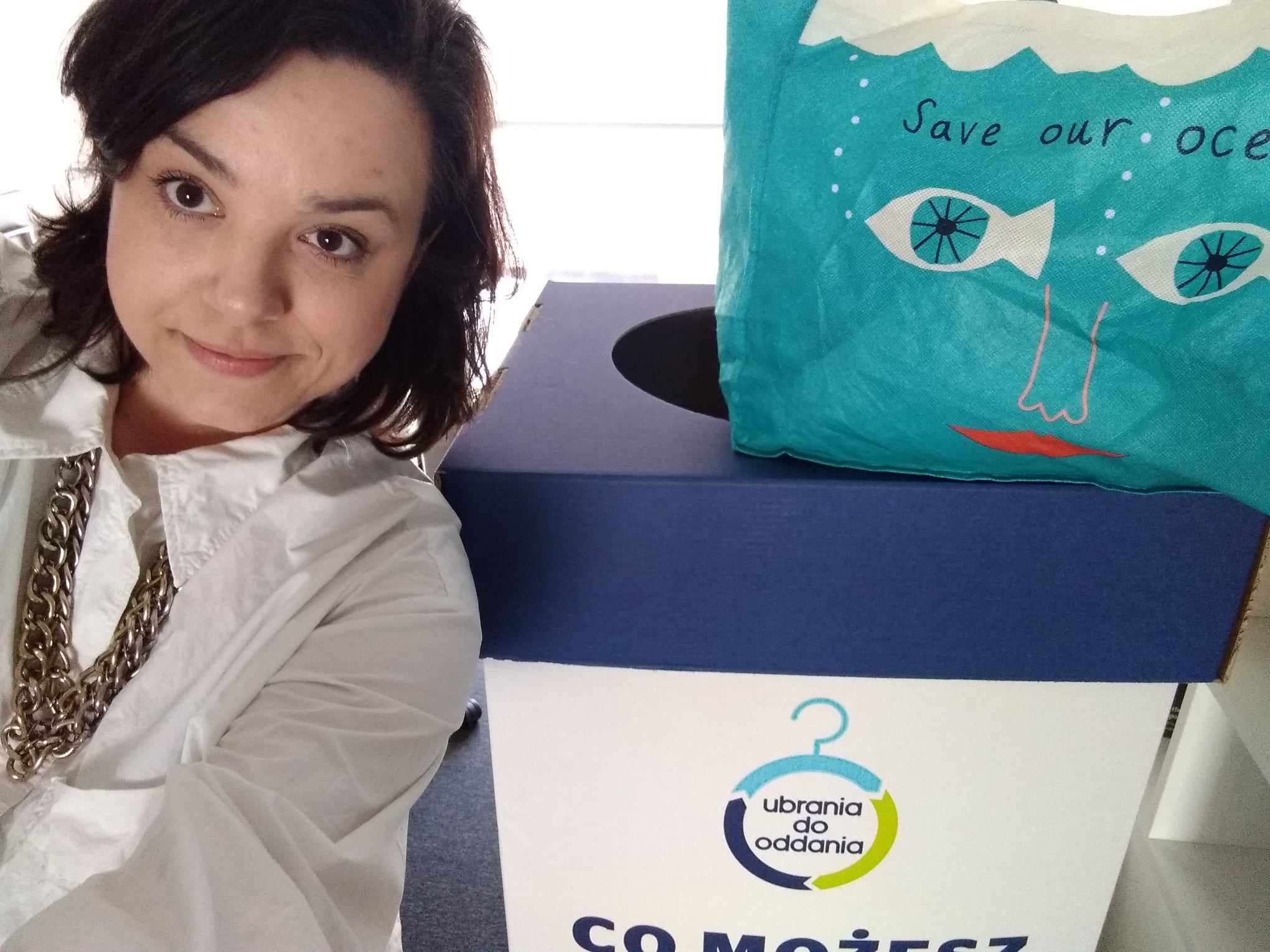 Marta robi selfie na tle pudełka z napisem "ubrania do oddania"
