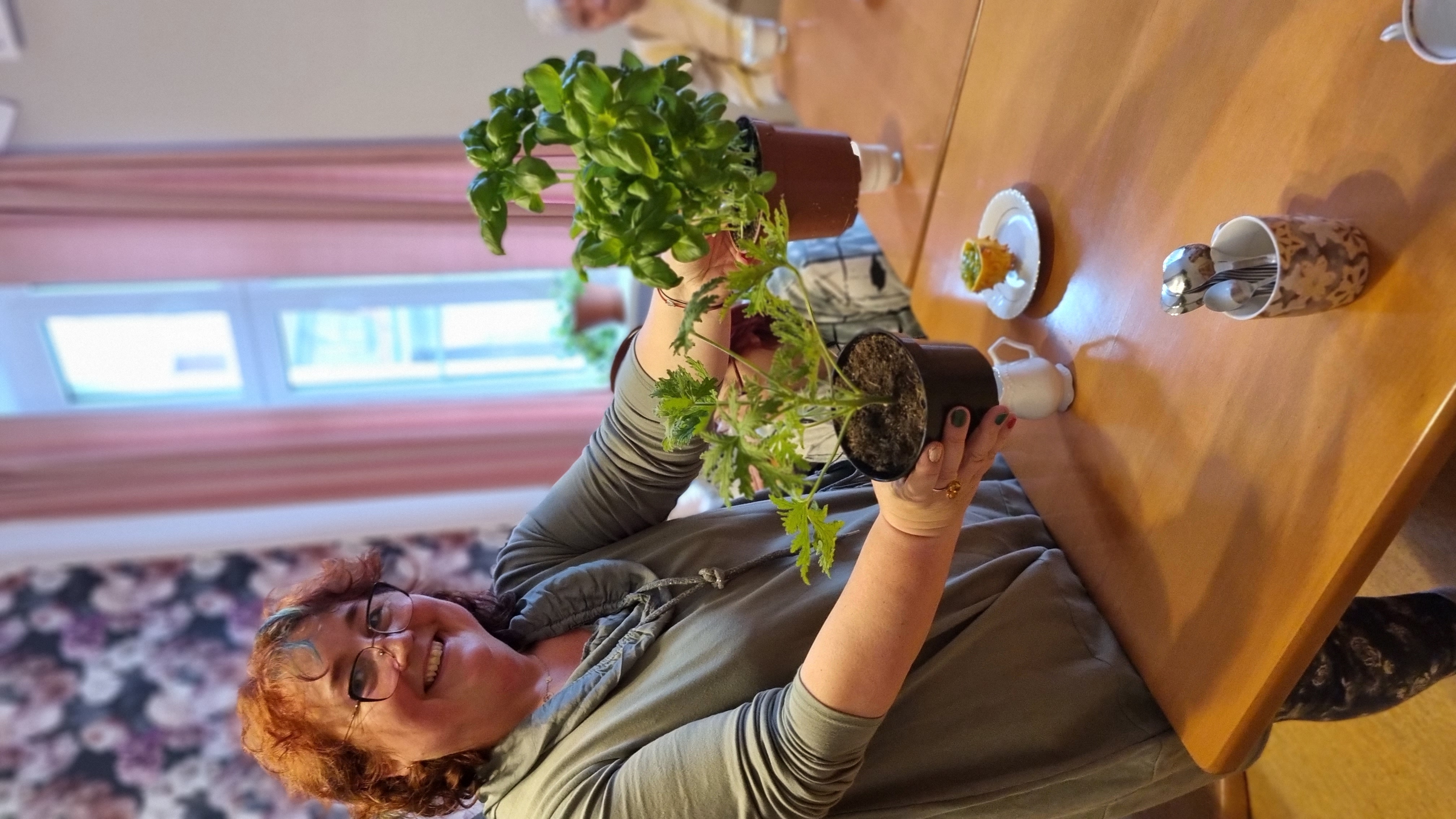 Kobieta trzyma w dłoniach sadzonki dwóch roślin. Uśmiecha się