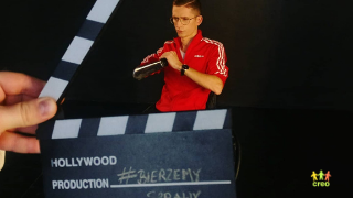 Na pierwszym planie otwarty klaps filmowy z napisem #bierzemy sprawy. Za nim widoczna osoba na wózku z protezą jednej ręki, która ma uniesione ręce w geście siły: pięść w dłoń.