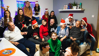 Grupa uśmiechniętych osób pozuje do zdjęcia. Na głowach mają czapki mikołaja, rogi renifera i inne świąteczne akcenty.