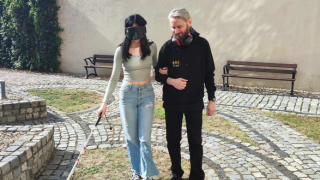 Mężczyzna w bluzie z logo CREO asystuje kobiecie z opaską na oczy. Kobieta porusza się z pomocą białej laski.