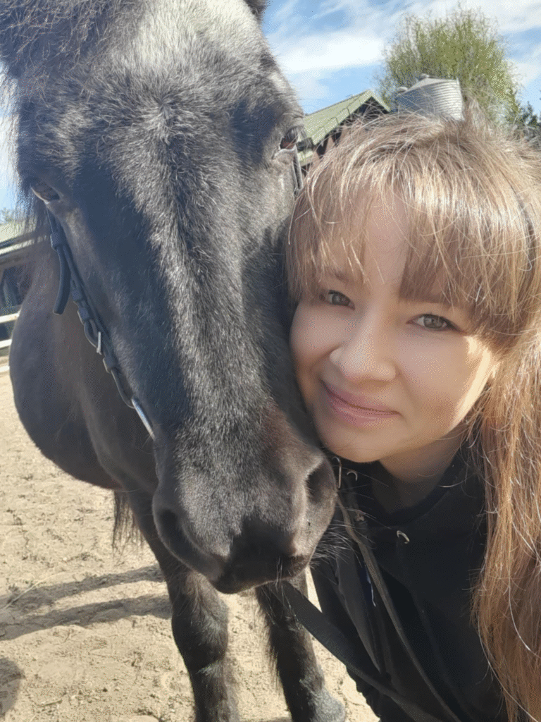 Maria przytulona do głowy czarnego konia