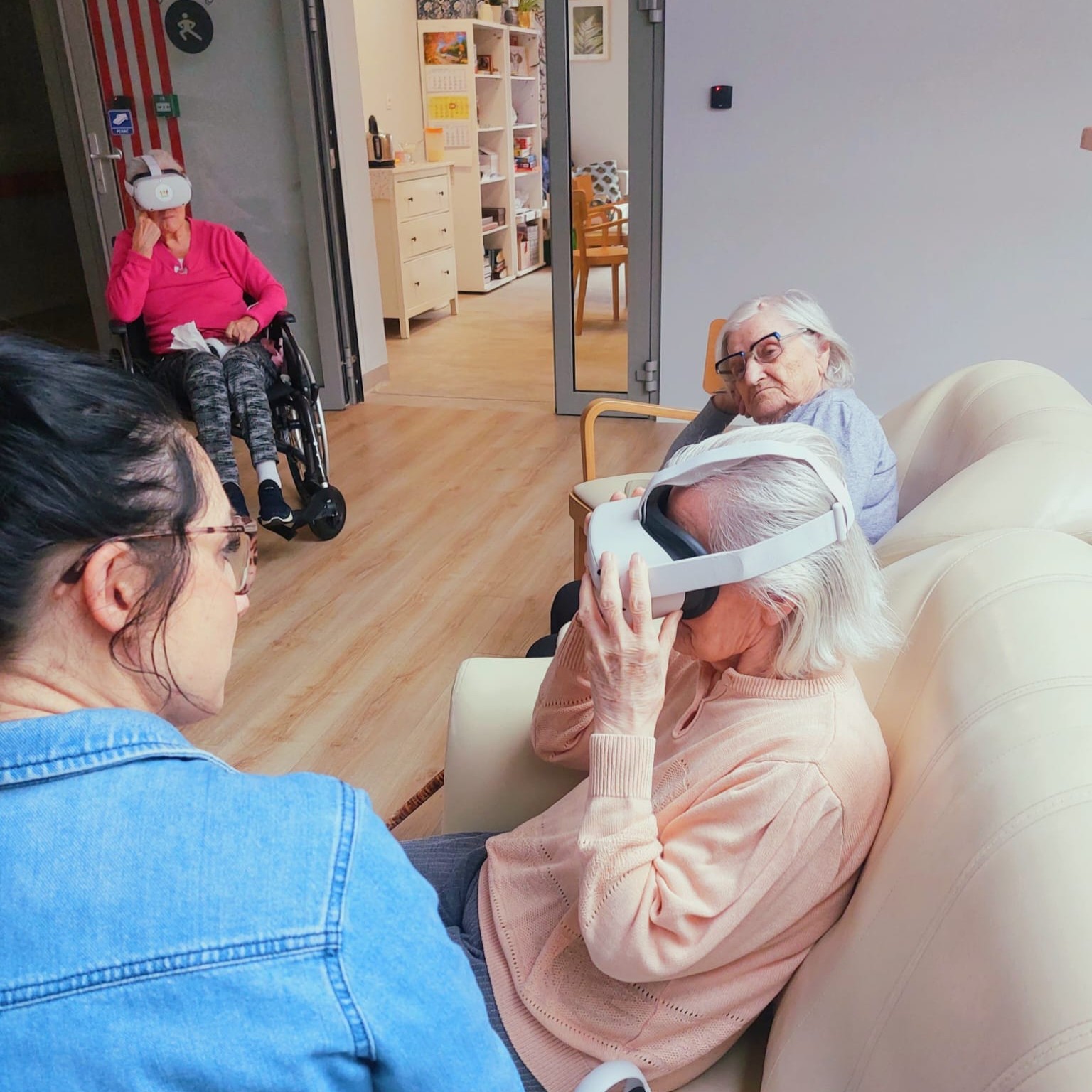 Warsztaty z wdrażania gogli VR. Trenerka siedzi na kanapie. Obok uczestniczka seniorka z goglami VR.