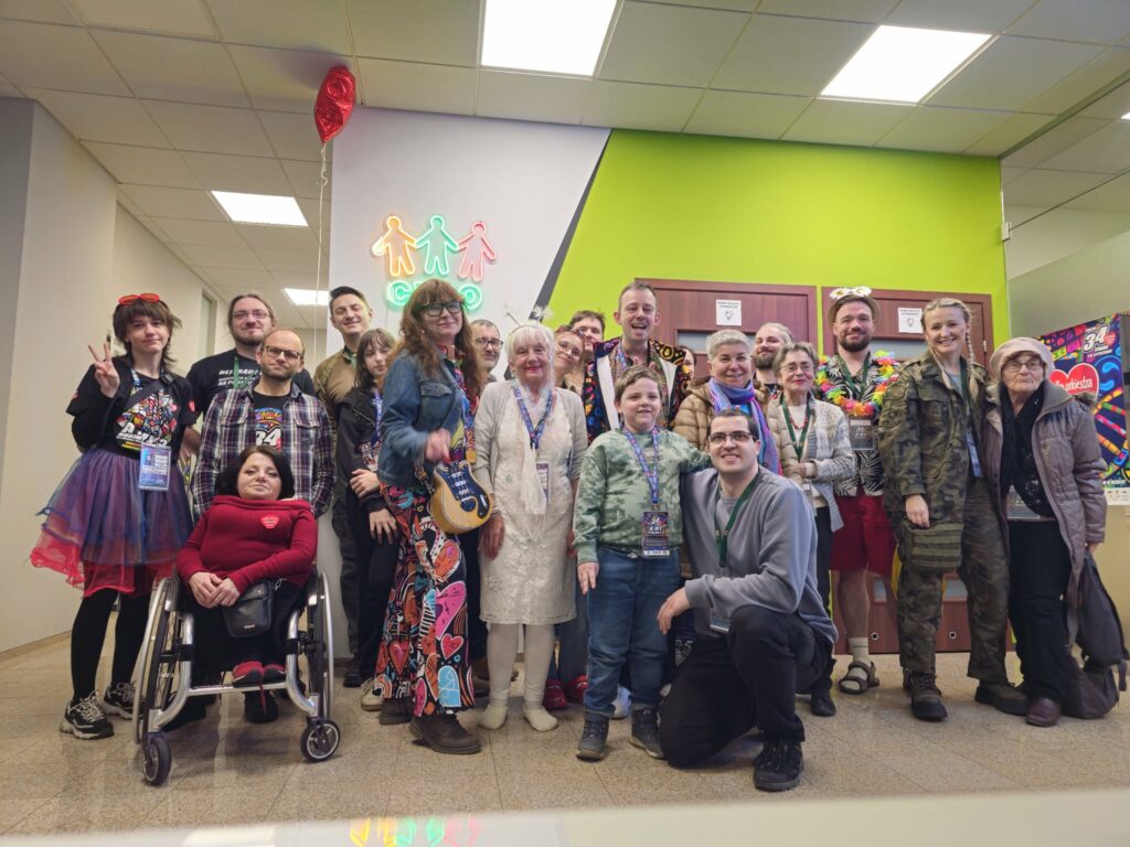 Grupa uśmiechniętych osób ubranych z identyfikatorami. Pozują w biurze, pod neonem CREO. W powietrzu balonik czerwone serduszko.